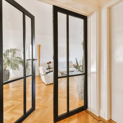 the inside of a house with wood flooring and black double doors leading to an open living room on one side